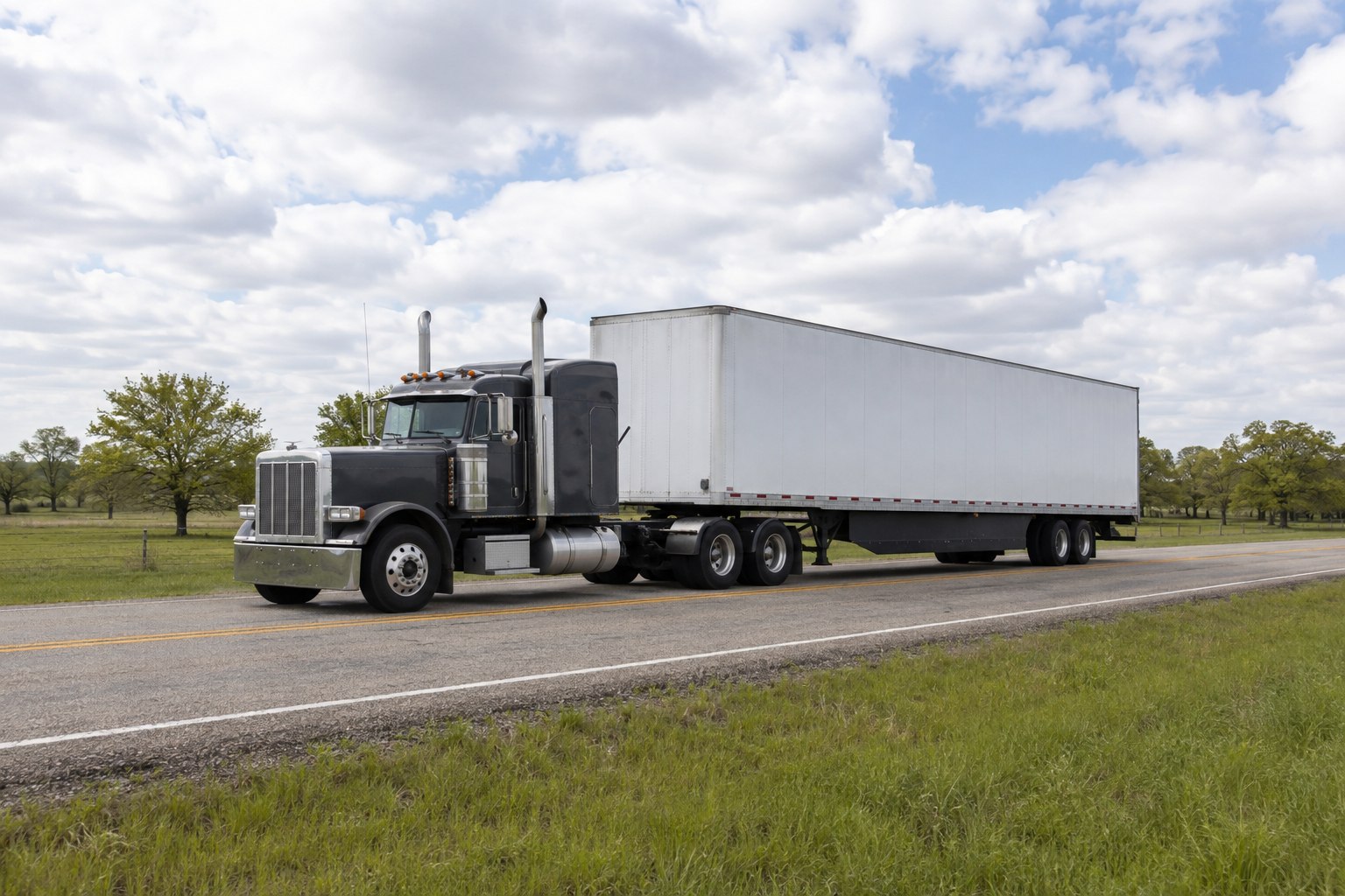An unbranded charcoal semi-truck and white trailer on a rural road